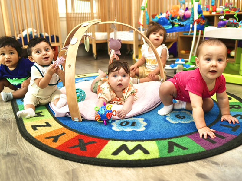 Five smiling babies playing together on an alphabet rug in the infant room