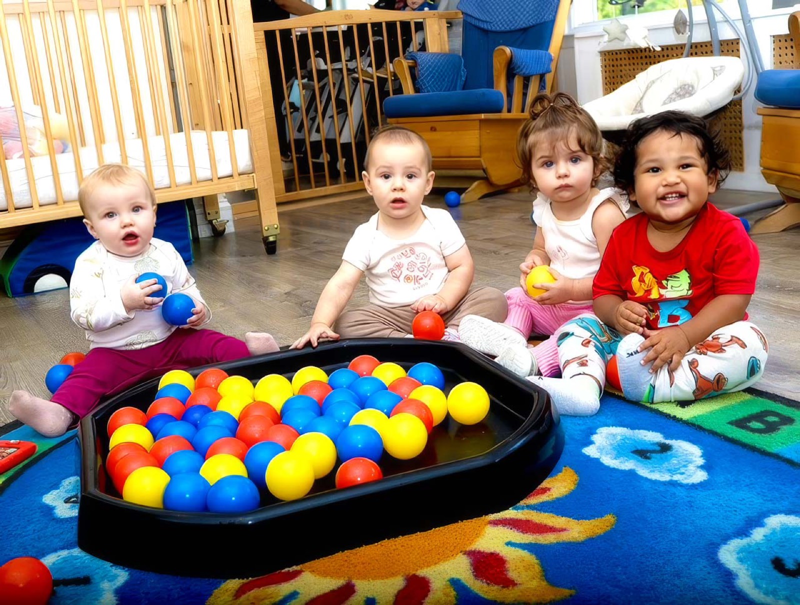 Four infants playing with coloured balls on the alphabet rug in the Pine Tree infant room