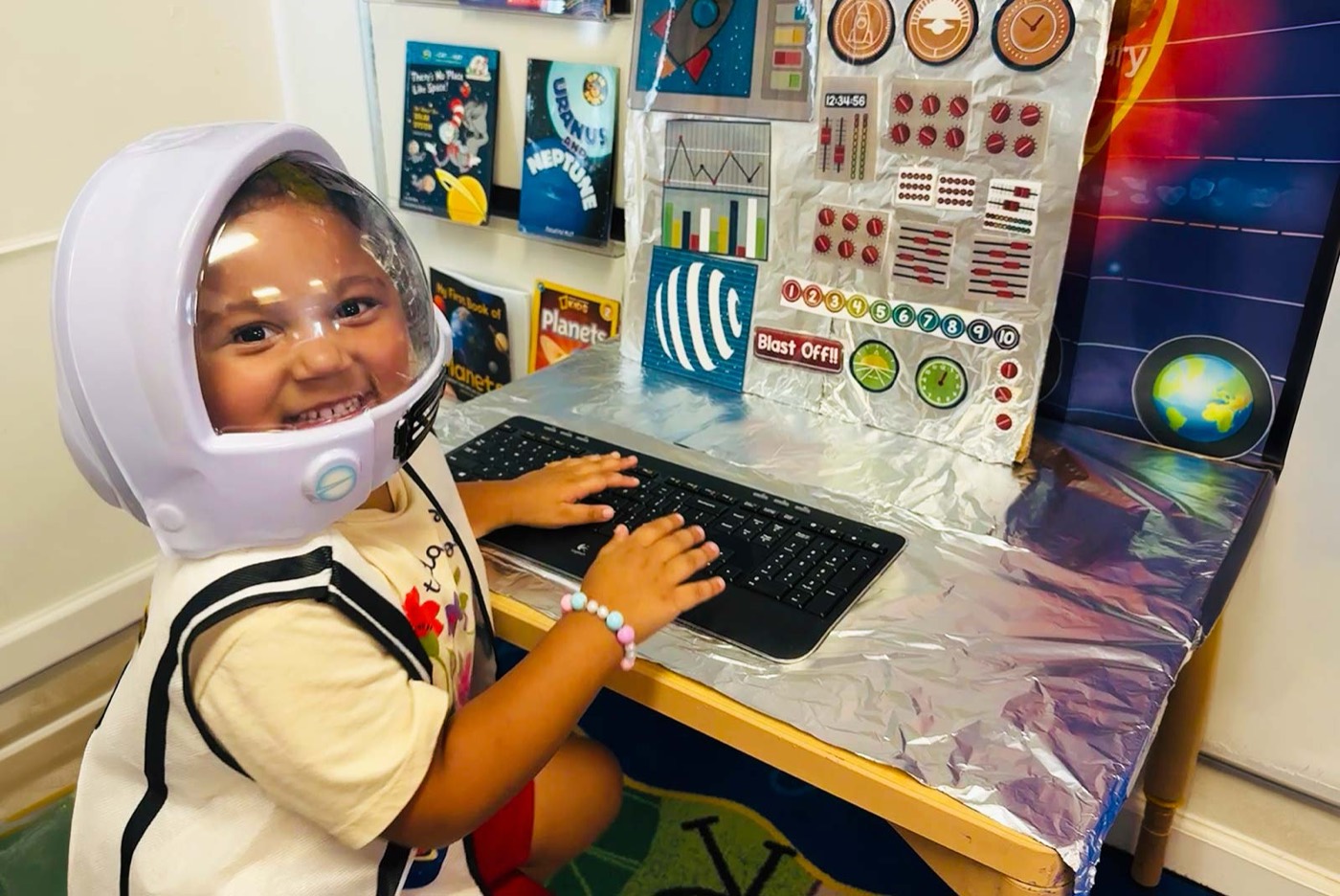 A child wearing an astronaut helmet using a computer at the Pre-K technology center