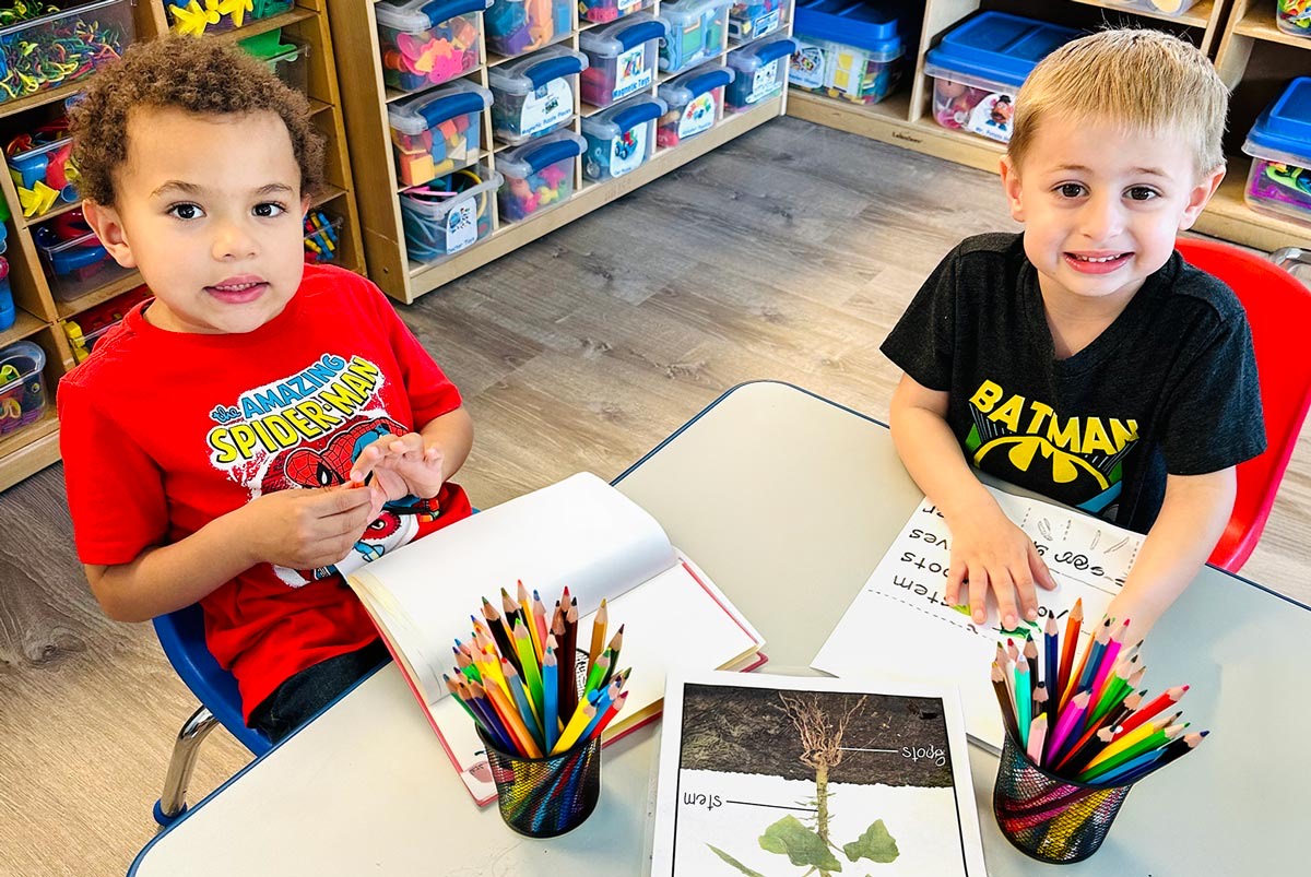 Two Pre-K children working with books and coloured pencils at a table
