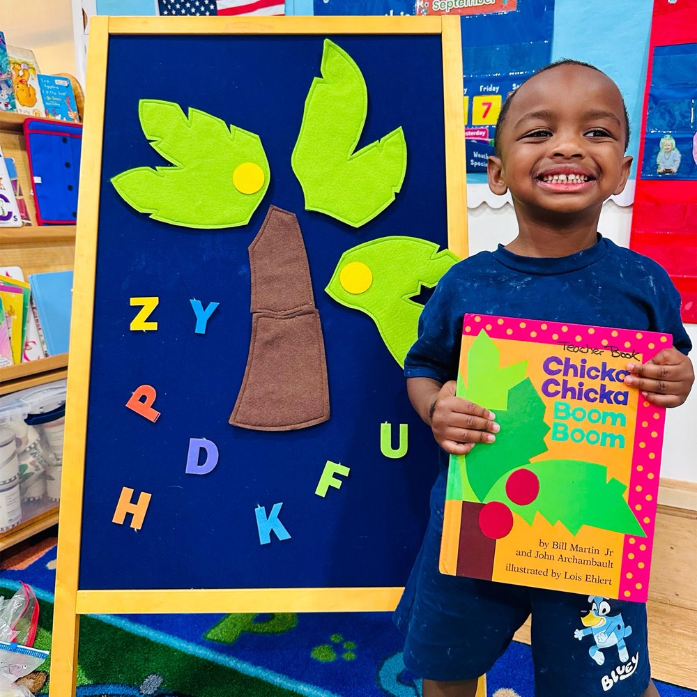 A preschooler holding the Chicka Chicka Boom Boom book beside a felt alphabet tree
