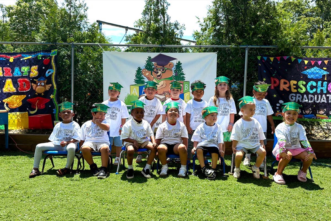 Preschool graduates in caps seated in front of a Pine Tree graduation banner