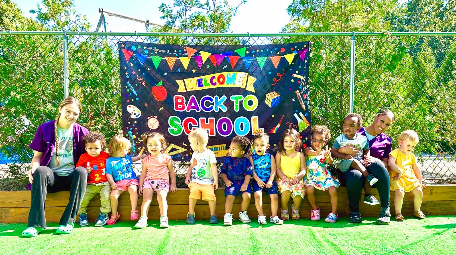 Toddlers and their teachers in front of a Welcome Back to School banner