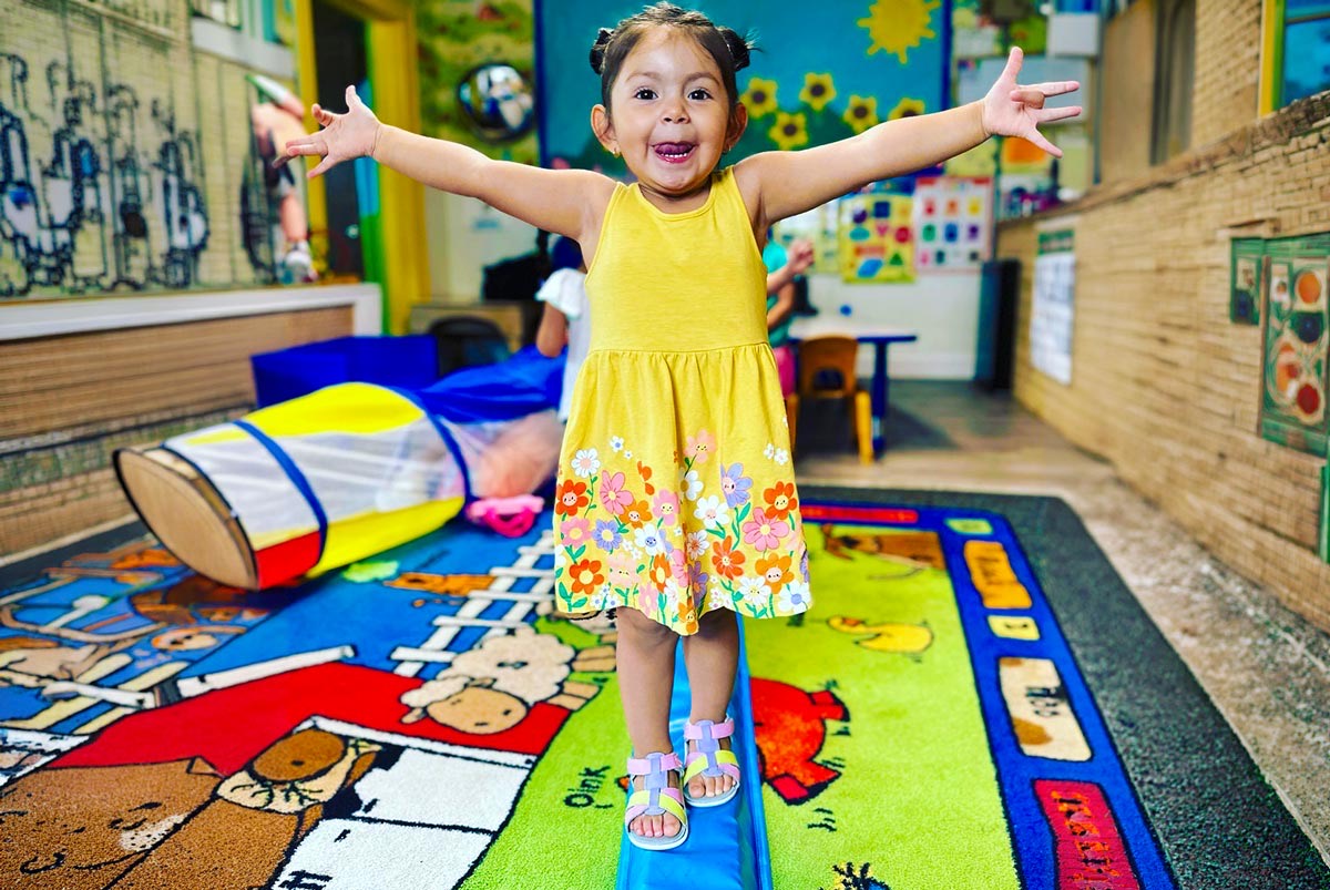 A toddler balancing along a beam with arms outstretched in the nursery room