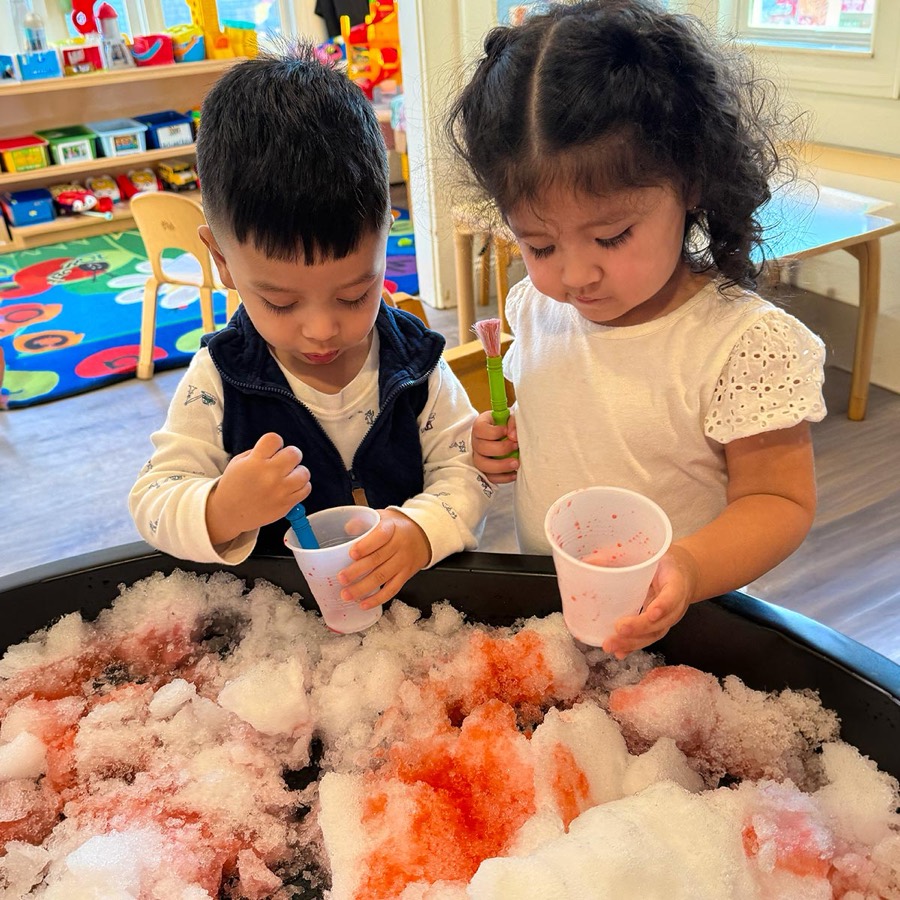Two toddlers exploring a coloured snow sensory bin together